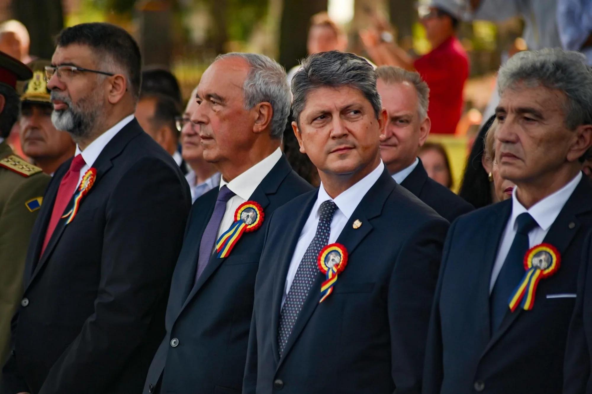 Titus Corlatean  and a  group of men in formal suits with ribbon badges attending a formal outdoor event.
